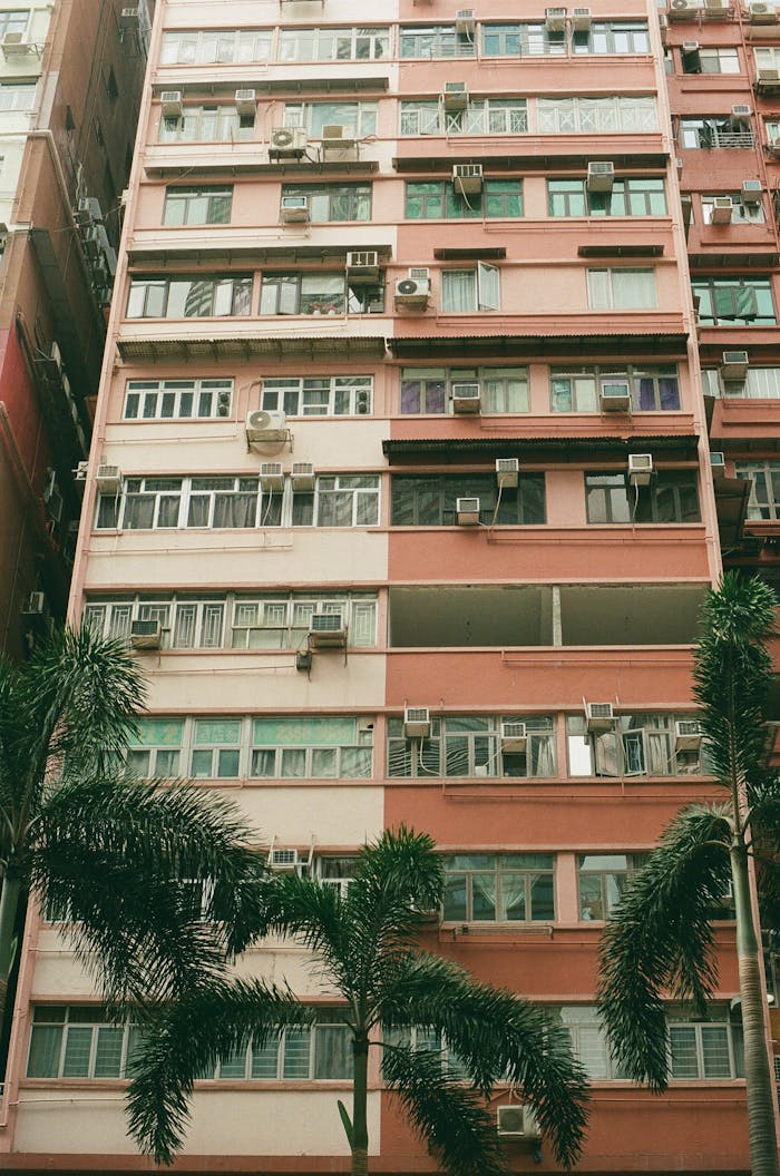 Vertical view of a high-rise apartment building with air conditioners and palm trees in the foreground.